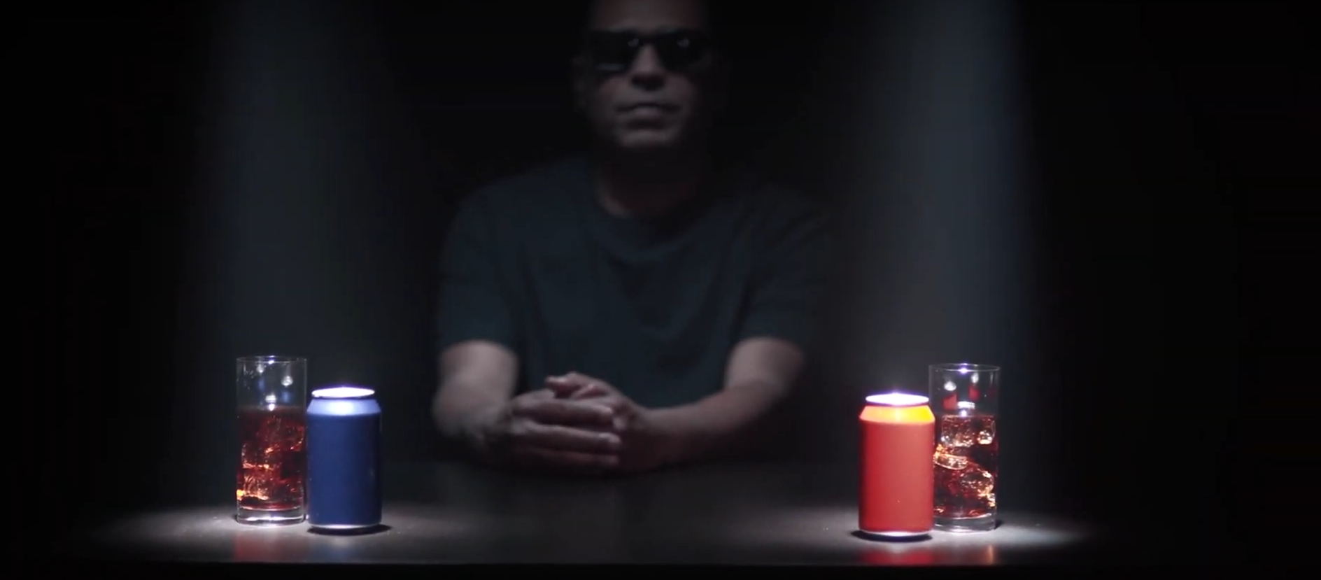 Homem de óculos escuros em frente a duas latas de refrigerante